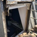 Image shows a dormer window stripped of its rotten sections, exposing the underlying frame before restoration.